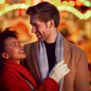 Couple Against City Lights Outdoors Wearing Coats And Scarves Enjoying Night Out Together
